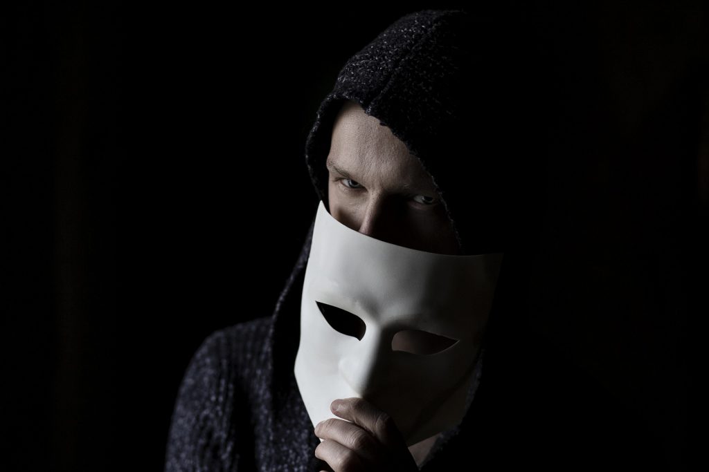 Man in hoodie peering over face mask